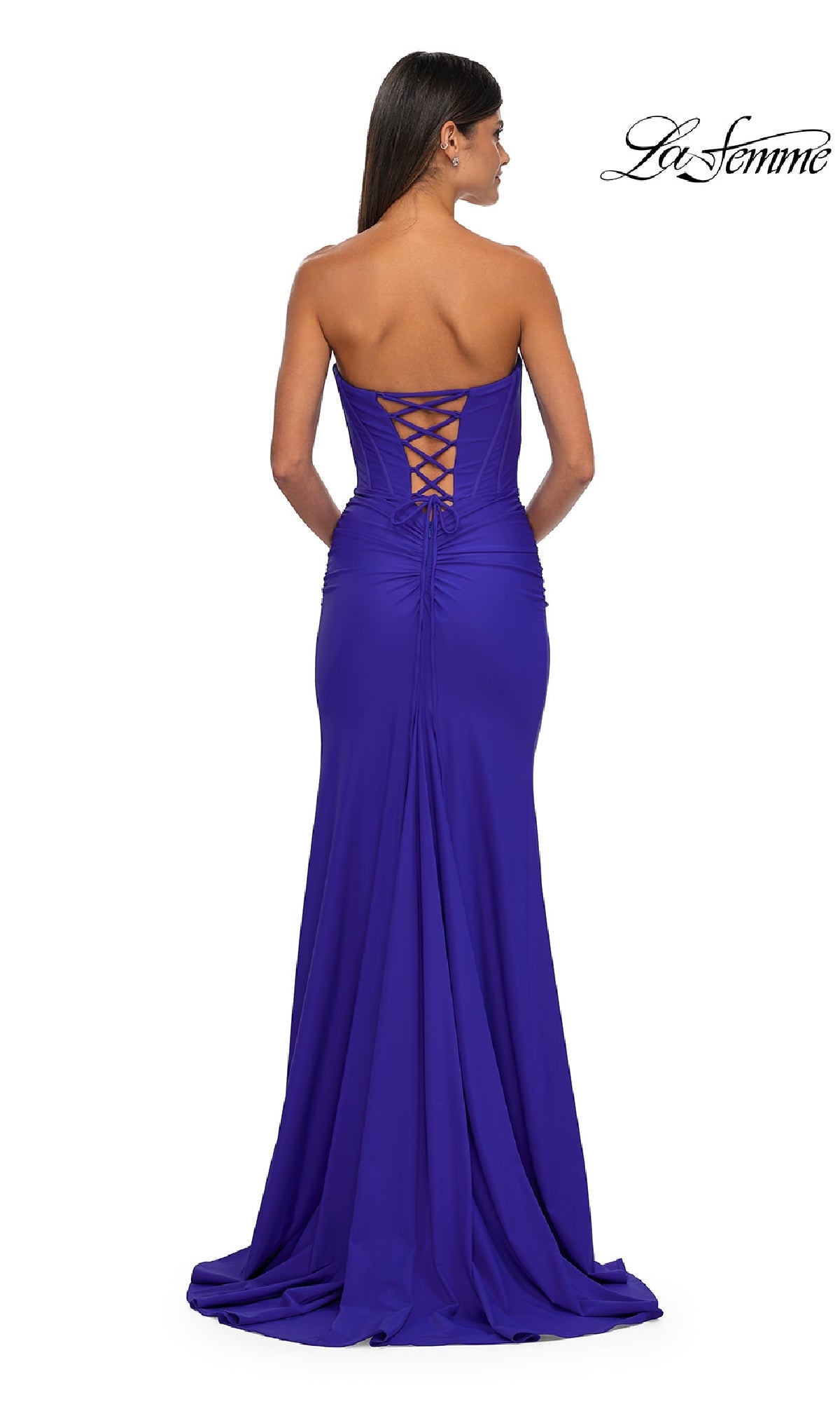 A woman in the Strapless Sweetheart Prom Gown: La Femme 32843, a royal blue floor-length dress with a corset back, stands facing away from the camera.